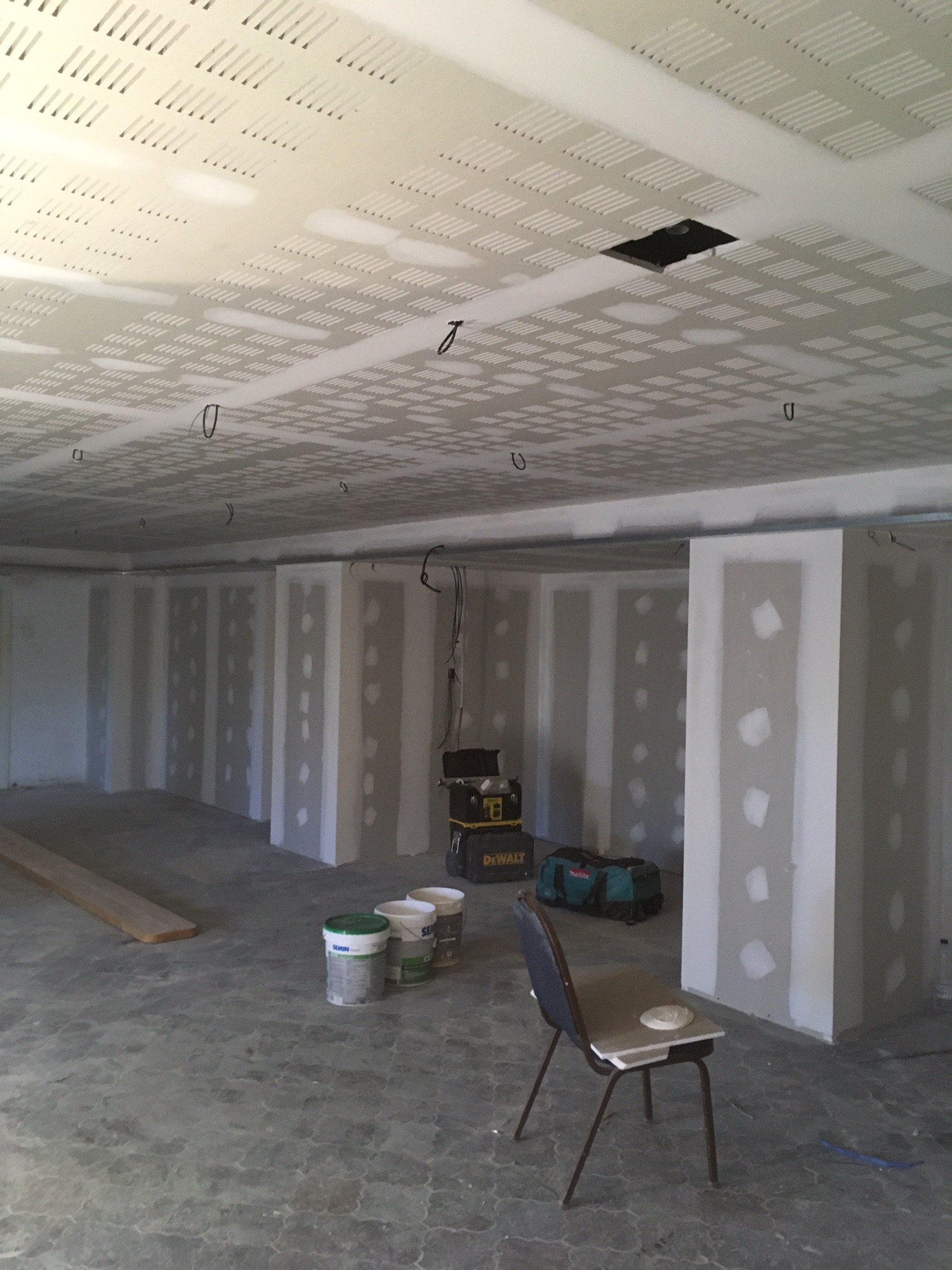 Montaż sufitu podwieszanego z perforowanej płyty gipsowo-kartonowej i ścian działowych w surowym stanie, widoczny otwór rewizyjny, narzędzia i materiały budowlane.