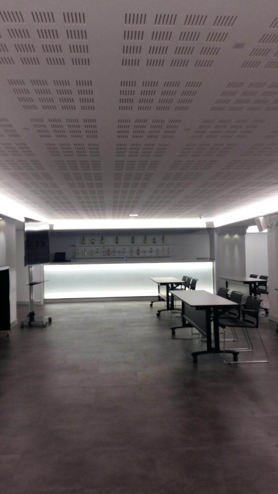 Sala konferencyjna z perforowanym sufitem podwieszanym, oświetleniem LED i minimalistycznym barem w tle.