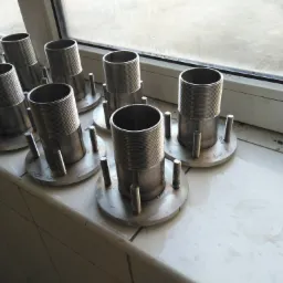 Szereg identycznych, metalowych elementów z gwintowanym cylindrem, okrągłą podstawą i trzema śrubami, ułożonych na białej, kafelkowanej powierzchni przy oknie.