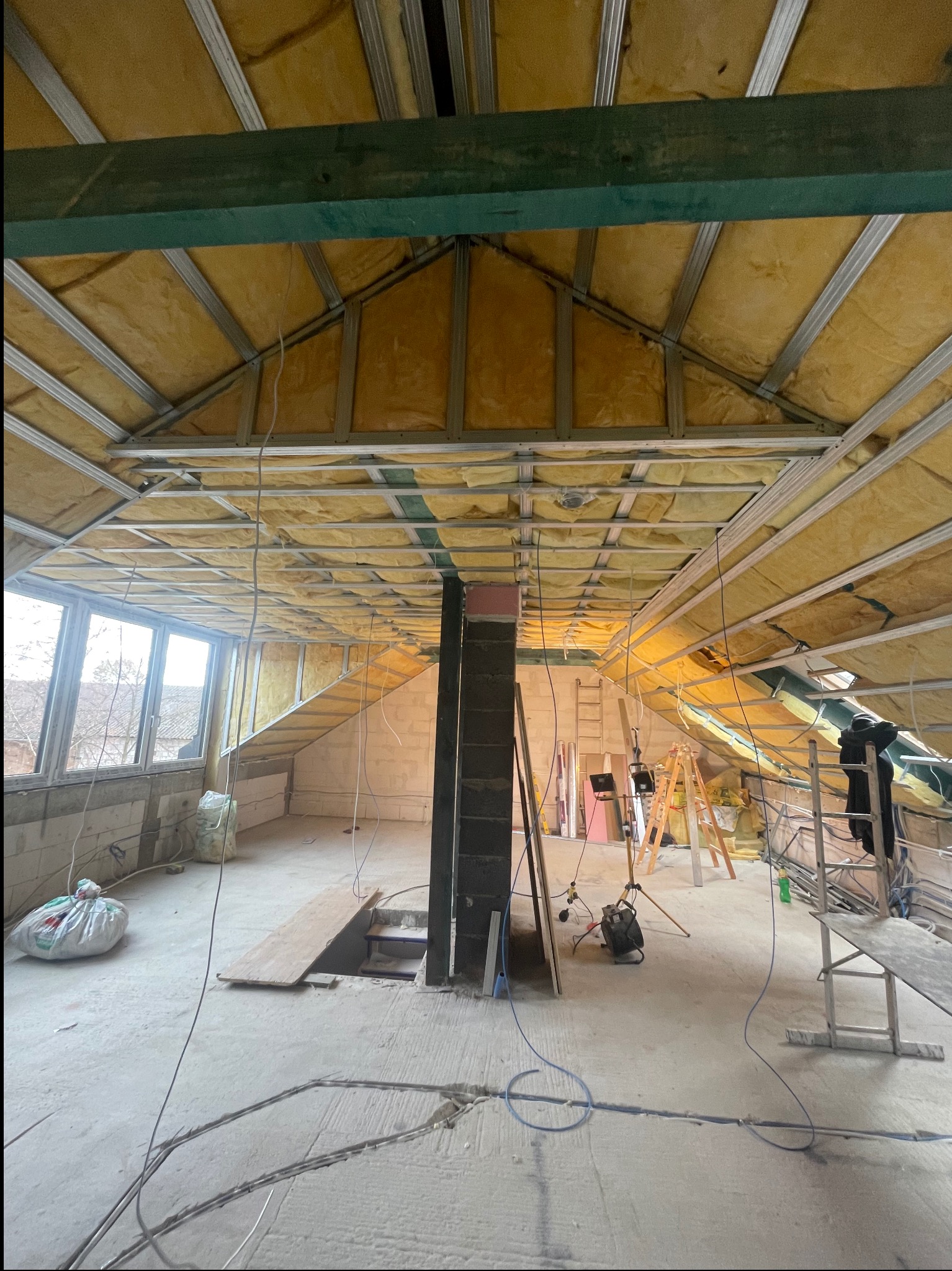 Poddasze w trakcie adaptacji: widok na konstrukcję sufitu z izolacją z wełny mineralnej, metalowy stelaż, okna dachowe i elementy instalacji elektrycznej.