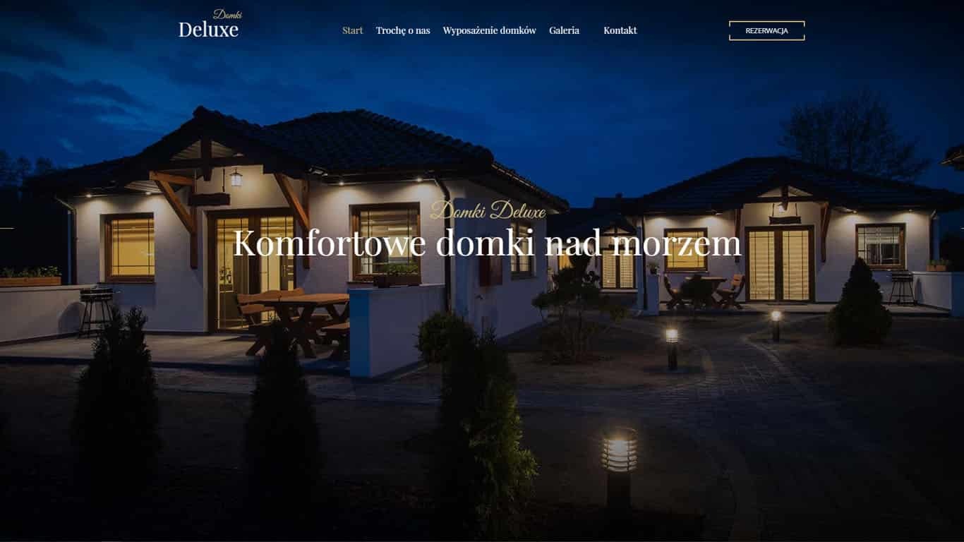 Zrzut ekranu strony internetowej Domki Deluxe prezentujący elewacje dwóch domków letniskowych oświetlonych nocą, z widocznym menu nawigacyjnym u góry.