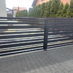 Nowoczesna, pozioma brama wjazdowa w kolorze antracytowym, zamontowana na posesji z kostką brukową i żywopłotem w tle.