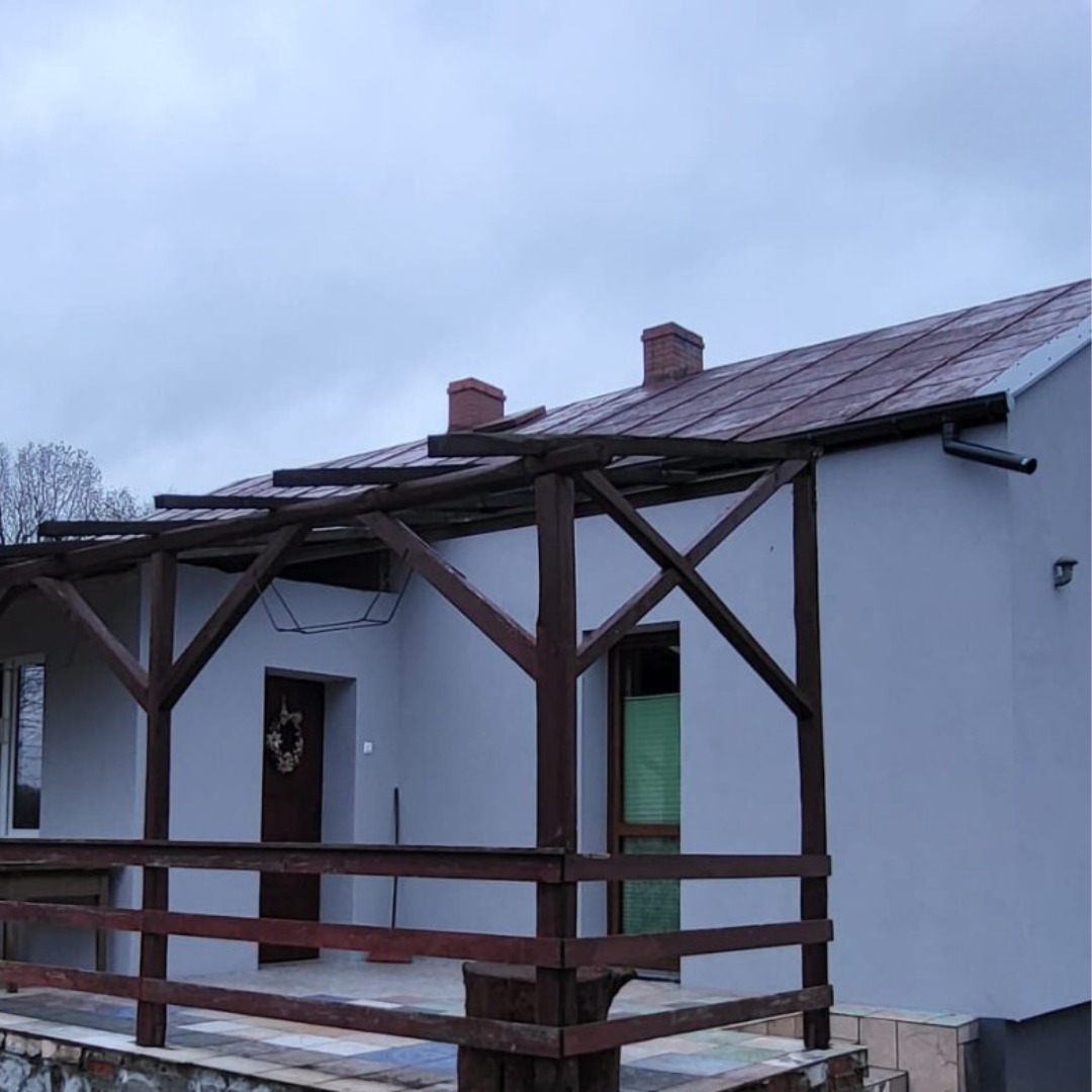 Dom jednorodzinny z drewnianą pergolą i nową elewacją w szarym kolorze, widoczne rynny i kominy