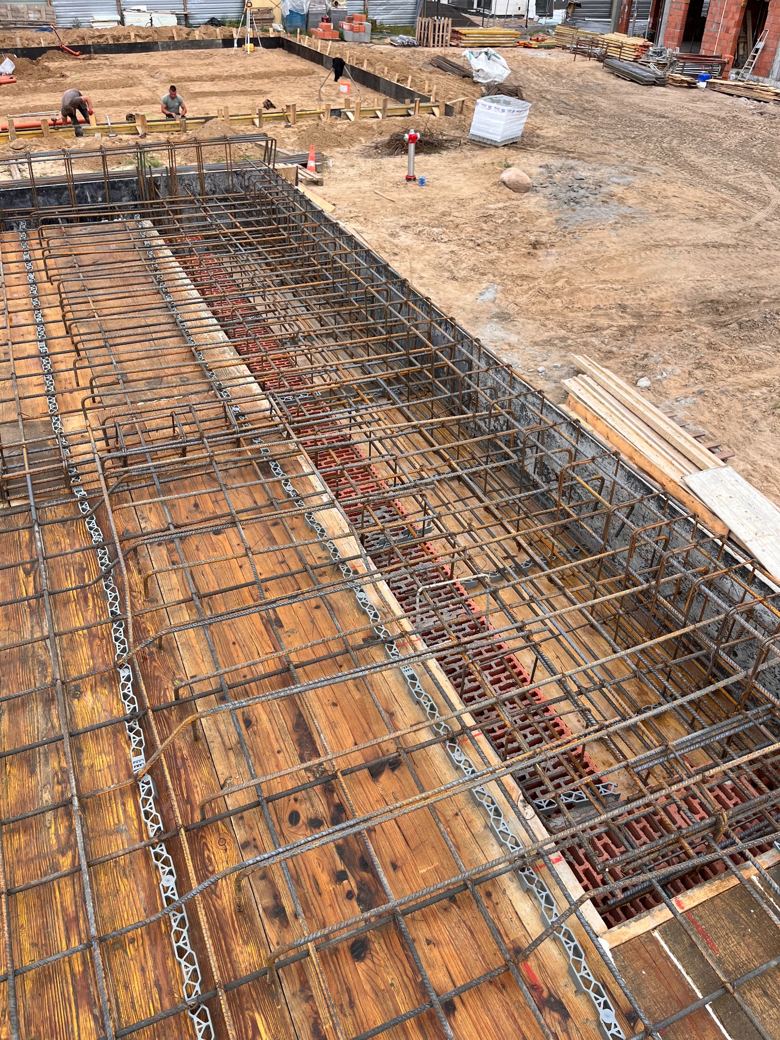 Zbrojenie fundamentu z drewnianym szalunkiem i dystansami z tworzywa sztucznego, widoczne przygotowania do zalewania betonem.