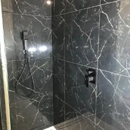 Nowoczesna kabina prysznicowa z czarnymi płytkami imitującymi marmur z białymi i złotymi żyłami, wyposażona w czarną armaturę i odpływ liniowy.