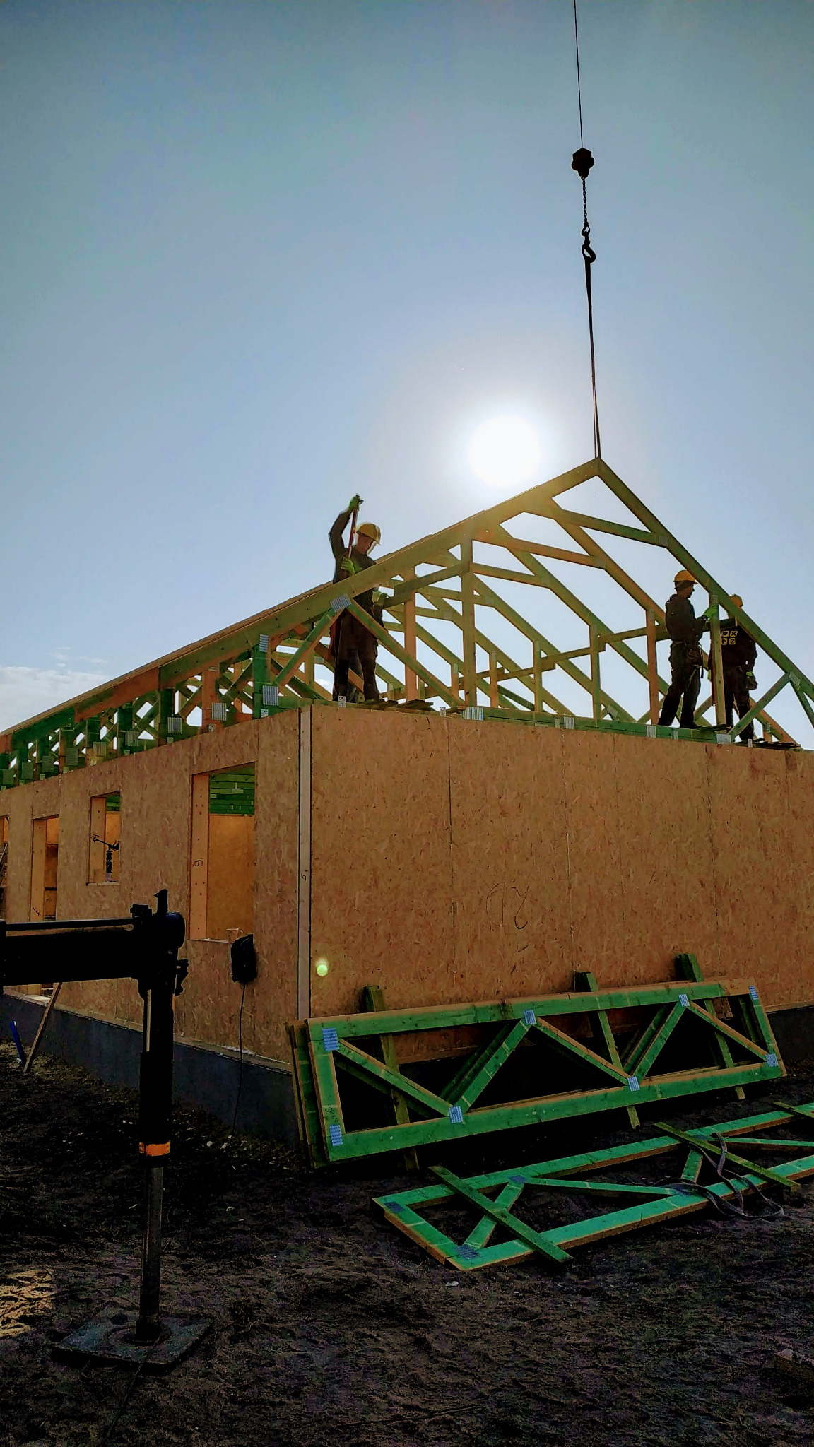 Montaż drewnianej konstrukcji dachu domu jednorodzinnego przez ekipę budowlaną, widoczny dźwig podnoszący elementy, ściany domu z płyt OSB, jasne niebo.