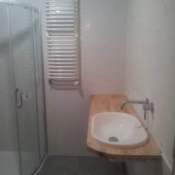 EUkalipt - Nowoczesna łazienka z kabiną prysznicową, grzejnikiem drabinkowym i umywalką nablatową na drewnianym blacie, widoczne ślady prac wykończeniowych na ścianie.