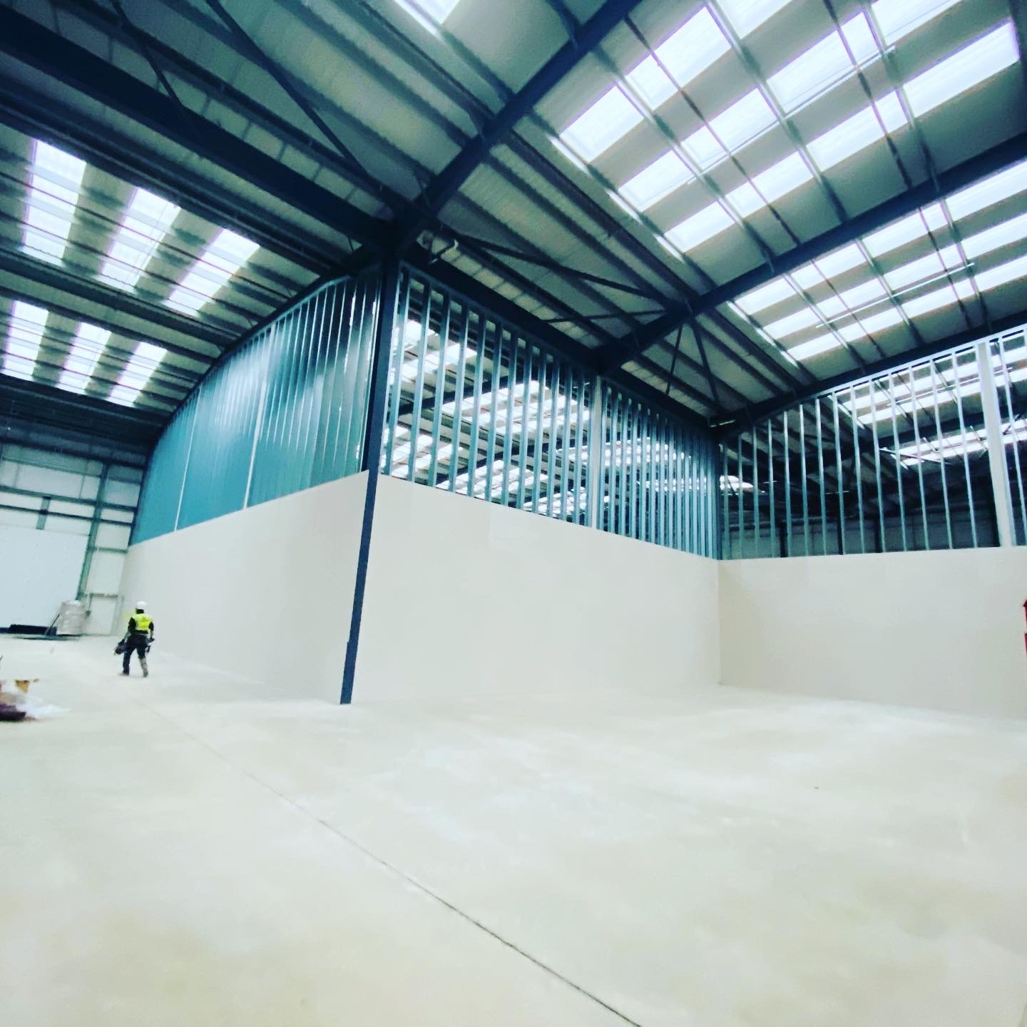 Wnętrze hali w Southampton w trakcie prac wykończeniowych, widoczna konstrukcja z profili stalowych pod płytę karton gips na ścianie, pracownik w oddali.