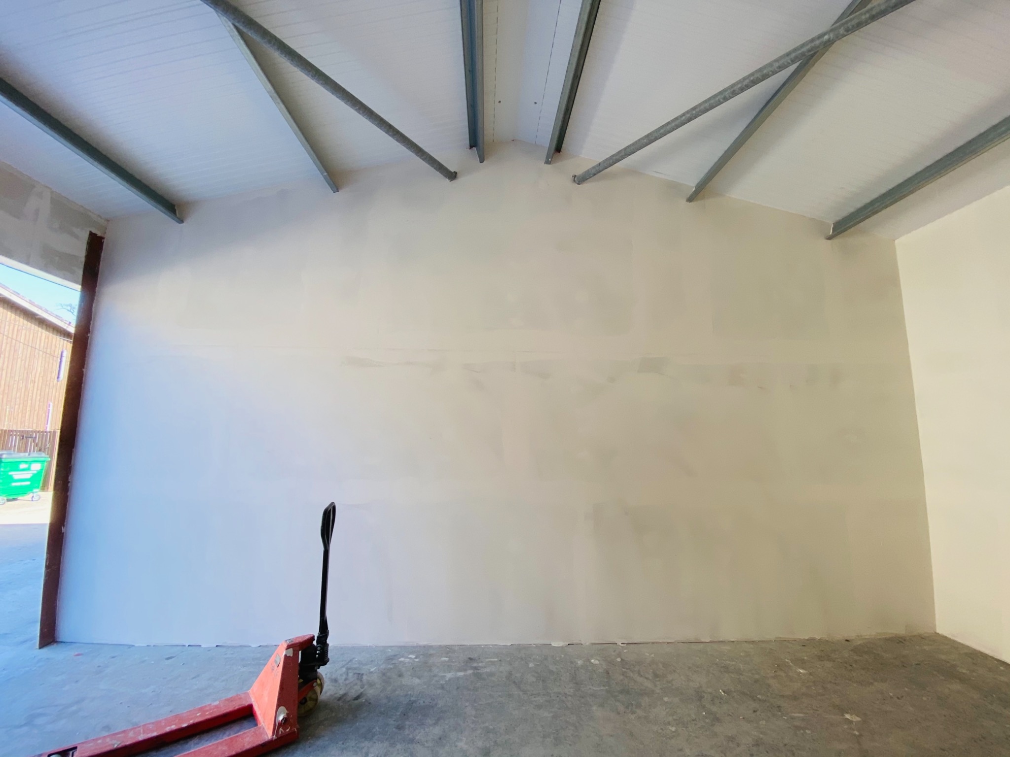 Wnętrze magazynu w trakcie przygotowania do malowania, ściany po szpachlowaniu, widoczny wózek paletowy.