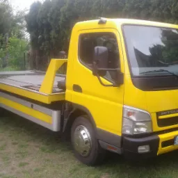 Żółta laweta Mitsubishi Fuso Canter zaparkowana na trawie, widoczna tablica rejestracyjna B1 017EA.