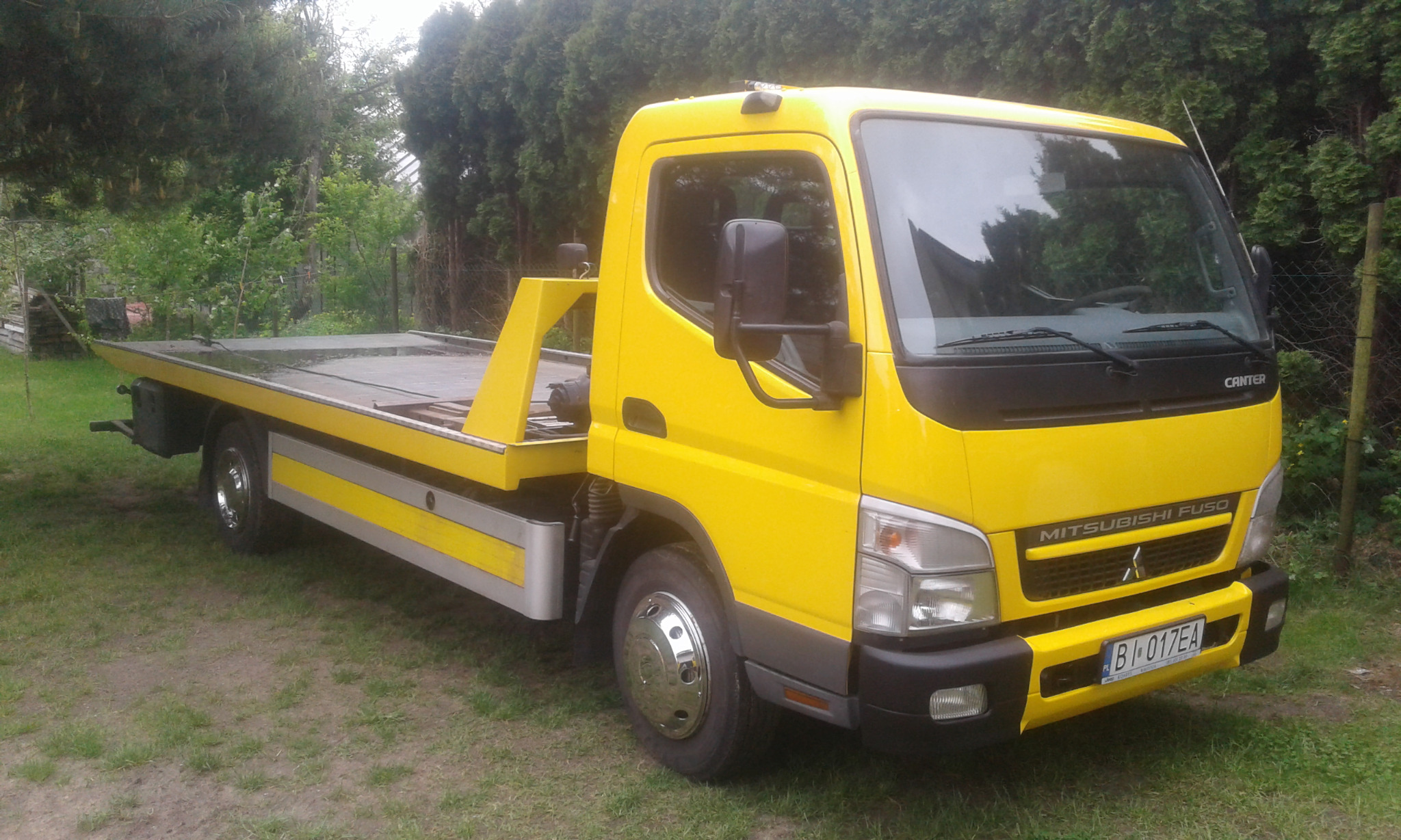 Żółta laweta Mitsubishi Fuso Canter zaparkowana na trawie, widoczna tablica rejestracyjna B1 017EA.