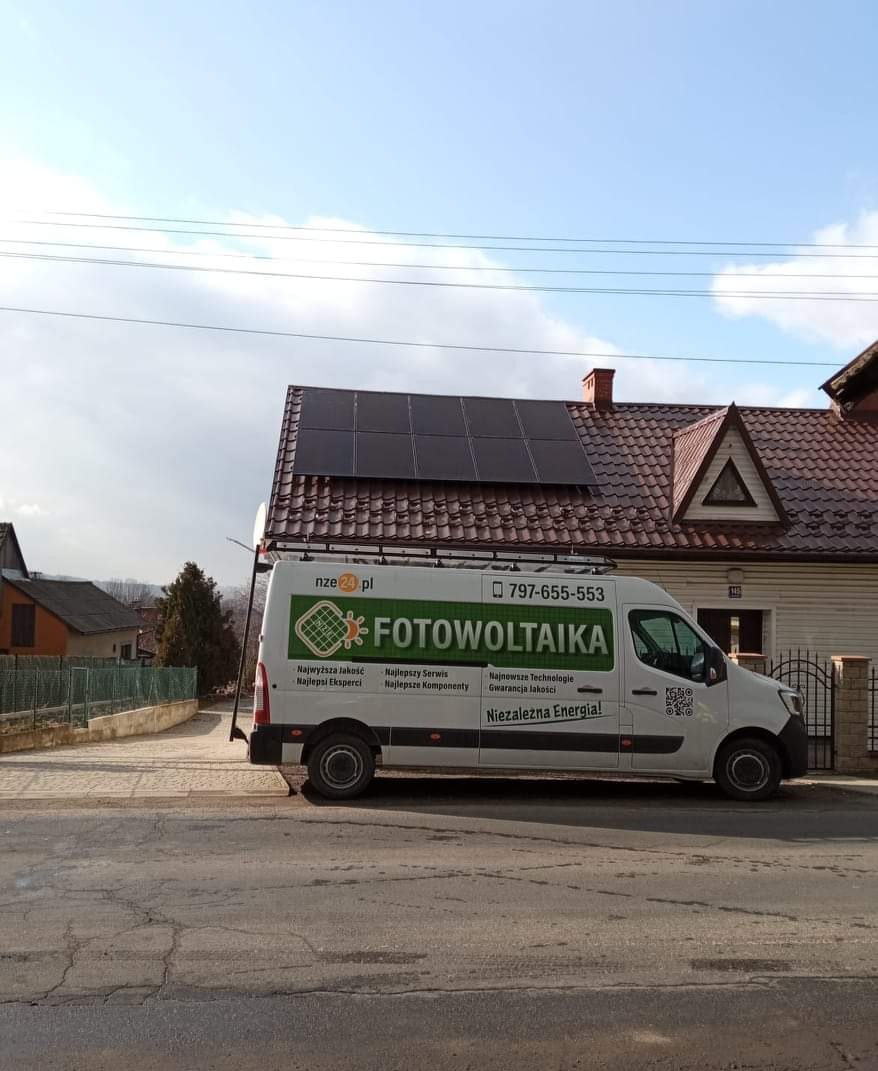 Panele słoneczne na dachu domu jednorodzinnego, widoczne z ulicy, z zaparkowanym firmowym vanem z logo instalatora.