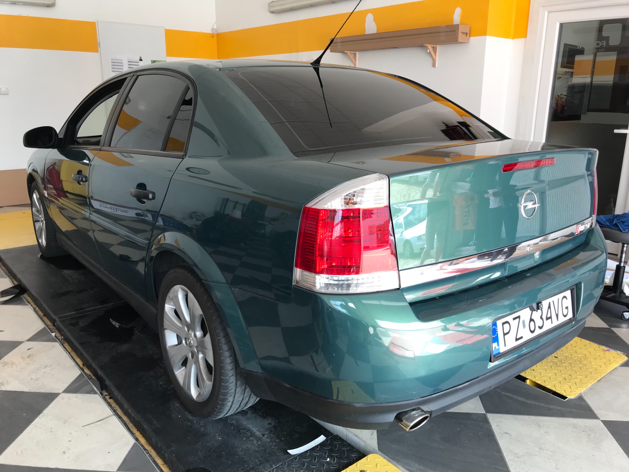 Zielony Opel Vectra po przyciemnieniu szyb, widoczny z tyłu na podnośniku w warsztacie, z polską tablicą rejestracyjną i anteną na dachu.