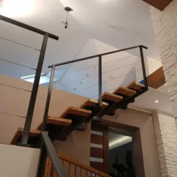 Drewniane schody z metalową balustradą i stalowymi linkami w nowoczesnym wnętrzu z dekoracyjną ścianą z kamienia.