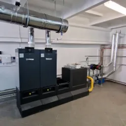 Dwa kotły grzewcze marki Buderus z podłączeniami kominowymi i instalacją hydrauliczną w pomieszczeniu kotłowni.