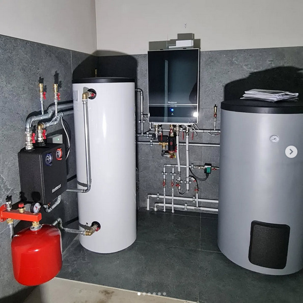 Kompletna instalacja grzewcza z kotłem kondensacyjnym Buderus, dwoma zbiornikami na wodę i osprzętem hydraulicznym w kotłowni wykończonej szarą płytką.