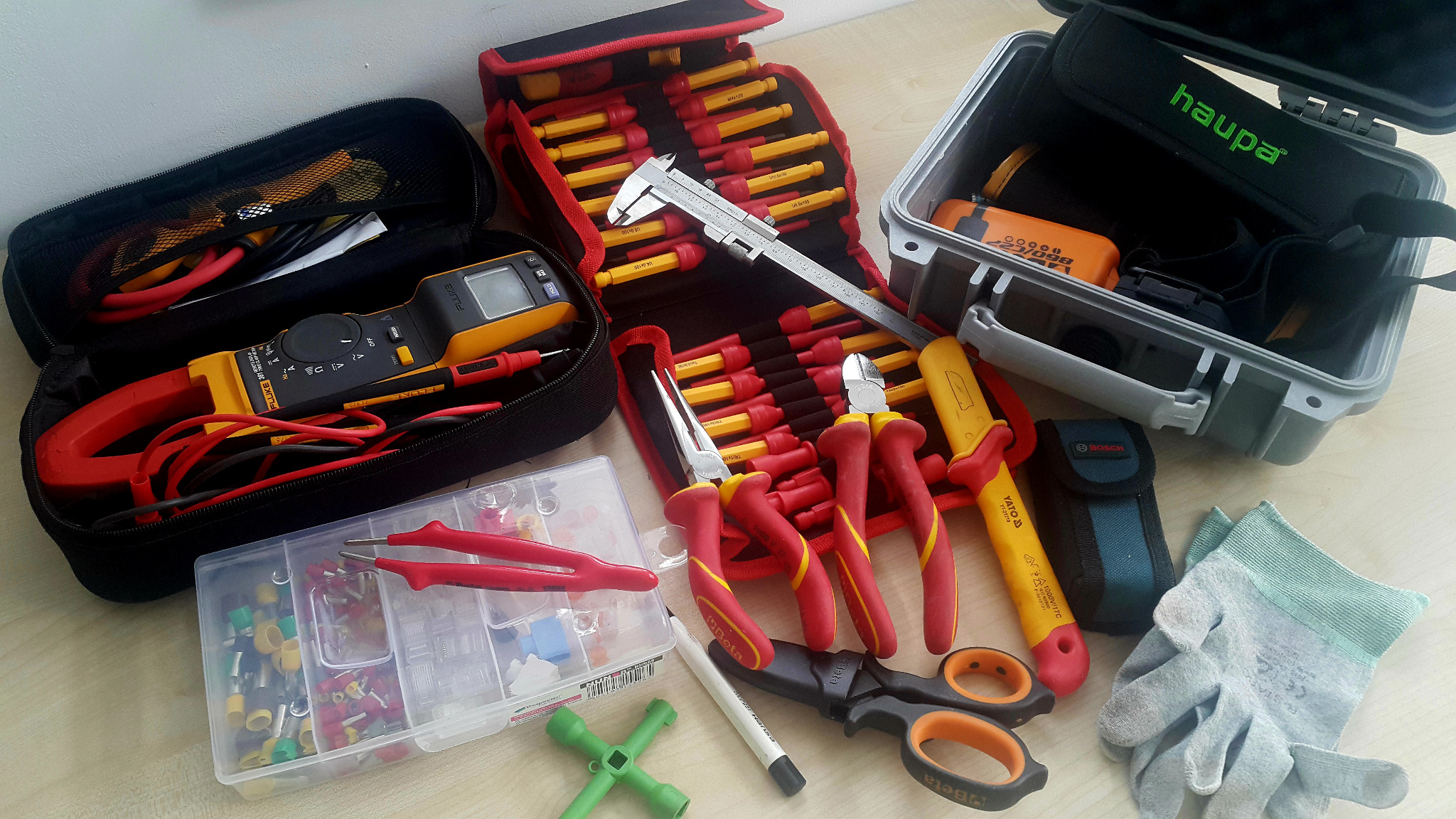 Zestaw narzędzi elektrycznych, w tym multimetr cęgowy Fluke, szczypce, wkrętaki z izolacją, ściągacz izolacji, obcinak do kabli Beta, tulejki kablowe, rękawice robocze i skrzynki narzędziowe Haupa...