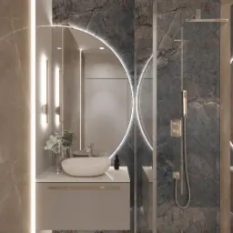 Nowoczesna łazienka z marmurowymi ścianami, okrągłym lustrem z podświetleniem LED, umywalką nablatową i szklaną kabiną prysznicową, oświetlona pionowymi lampami ściennymi.