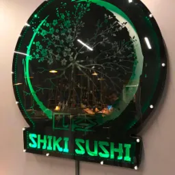 Podświetlany szyld restauracji Shiki Sushi z motywem drzewa wiśni, zamontowany na ścianie.