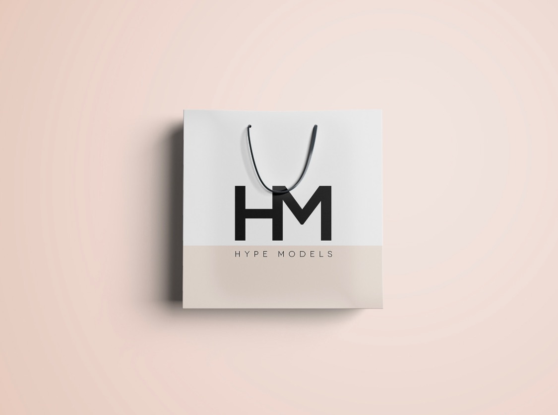 Biała torba papierowa z czarnym logo 'HM' i napisem 'HYPE MODELS' na beżowym tle, minimalistyczny design.