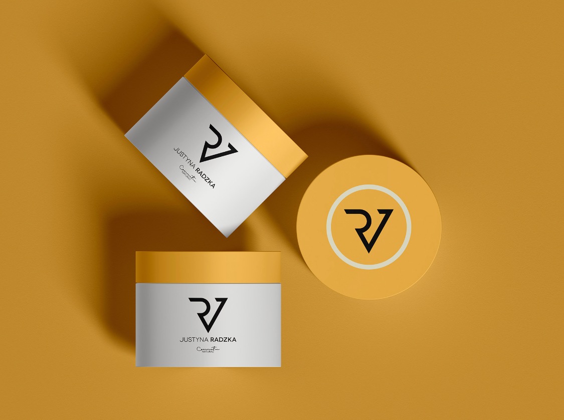 Trzy opakowania kosmetyków w odcieniach bieli i złota, z minimalistycznym logo na jednolitym, musztardowym tle, prezentowane w perspektywie z góry.