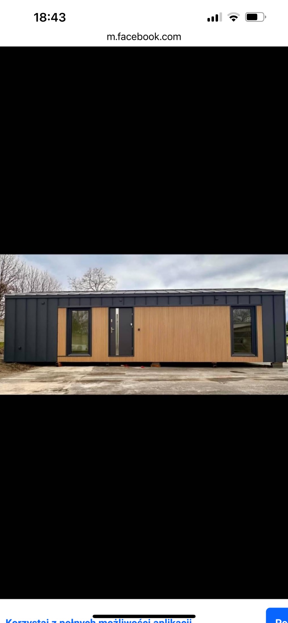 Nowoczesny dom modułowy z elewacją z pionowych paneli drewnianych i ciemnoszarej blachy, widoczny z zewnątrz, na betonowych podporach.