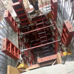 Zalewanie betonem szalunku fundamentowego z widocznymi zbrojeniami i elementami konstrukcyjnymi, częściowo wypełnione wodą.