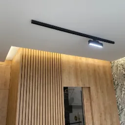 Nowoczesna łazienka w Straszynie z drewnianą okładziną ścienną, czarnym oświetleniem szynowym i widocznym fragmentem kabiny prysznicowej z czarno-białymi płytkami.