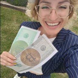 FUN-Dżasta Animator Justyna Potulicka - Uśmiechnięta kobieta w kapeluszu i okularach, trzymająca w rękach rekwizyty: banknoty dolarowe z wizerunkiem Bitcoin, na tle trawy i lawendy.