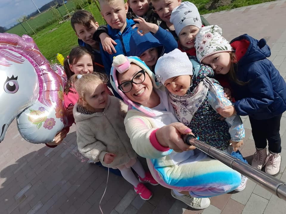 Zdjęcie grupowe z animatorką w kostiumie jednorożca i grupą dzieci, trzymane są balony w kształcie jednorożca, selfie zrobione z użyciem kijka.