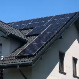 Czarny panel słoneczny na ciemnoszarym dachu domu jednorodzinnego z białymi ścianami w słoneczny dzień.