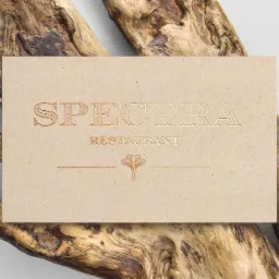 Beżowa wizytówka restauracji 'Spectra' z tłoczonym logo, ułożona na naturalnym kawałku drewna.