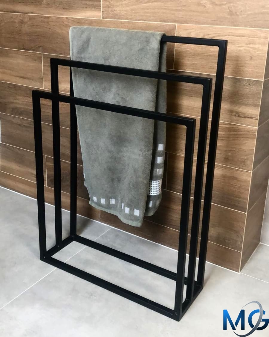 Czarny, metalowy stojak na ręczniki w stylu loft, z szarym ręcznikiem z białymi kwadratami, na tle płytek imitujących drewno.