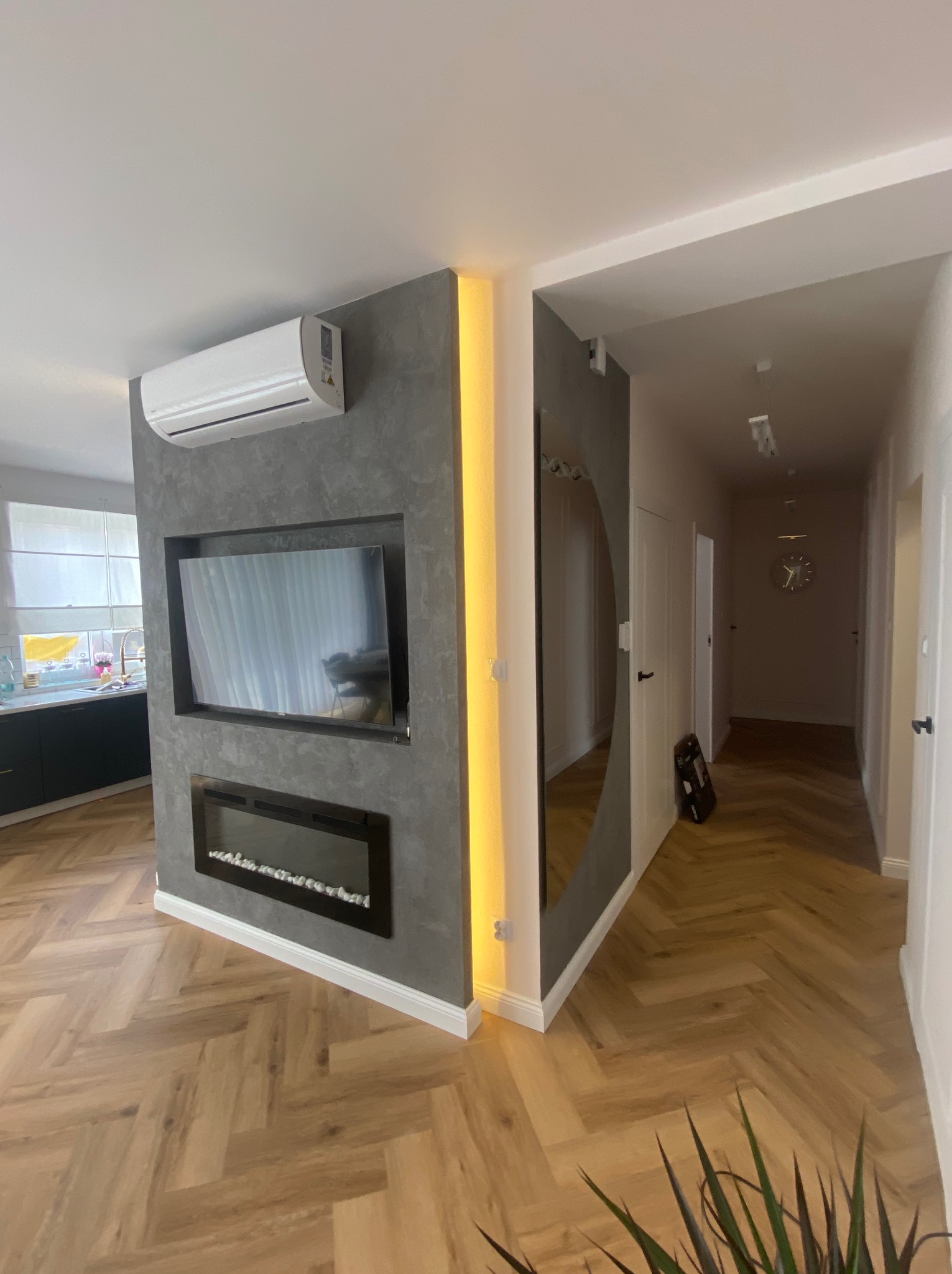 Nowoczesne wykończenie wnętrza: ściana z telewizorem i kominkiem elektrycznym, parkiet w jodełkę, klimatyzator, oświetlenie LED i lustro w przedpokoju.