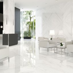 BUD MAX USŁUGI REMONTOWO BUDOWLANE ŁUKASZ CHRZAN - Błyszcząca, marmurowa podłoga w przestronnym holu recepcyjnym z białymi skórzanymi fotelami, szklanymi stolikami, czarną recepcją i widokiem na zieleń za oknem.