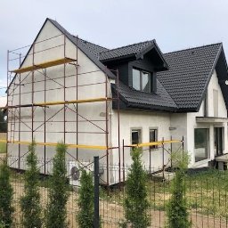 BUD MAX USŁUGI REMONTOWO BUDOWLANE ŁUKASZ CHRZAN - Dom jednorodzinny w trakcie ocieplania elewacji, widoczne rusztowania i surowa elewacja, czarny dach z dachówki.