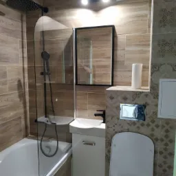 Nowoczesna łazienka z drewnopodobnymi płytkami, czarną armaturą i podtynkową spłuczką WC.