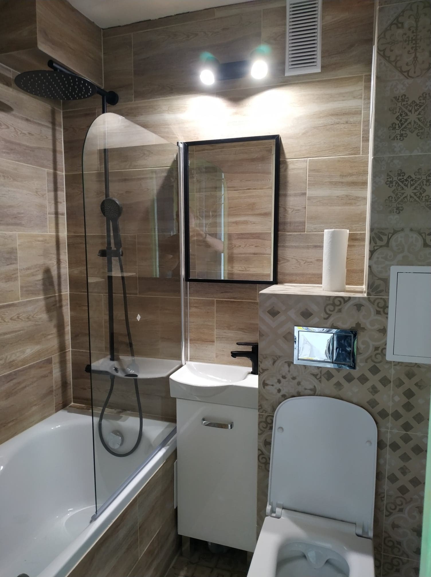 Nowoczesna łazienka z drewnopodobnymi płytkami, czarną armaturą i podtynkową spłuczką WC.