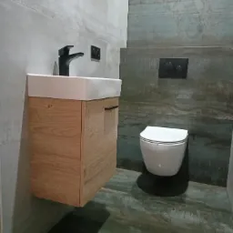 Nowoczesna łazienka z wiszącą toaletą, umywalką nablatową na drewnianej szafce i szaro-zielonymi płytkami imitującymi drewno na podłodze i ścianie