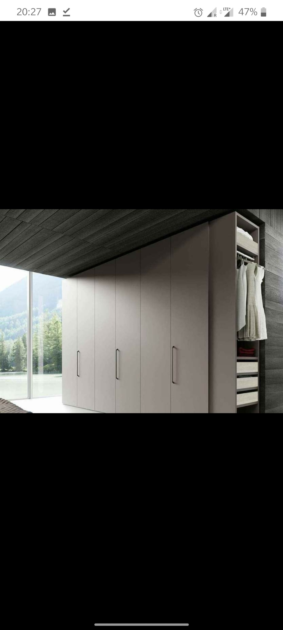 Zamknięta szafa z przesuwnymi drzwiami w kolorze taupe, z otwartą boczną sekcją ukazującą wieszaki z ubraniami i półki z tekstyliami, na tle panoramicznego okna z widokiem na las.