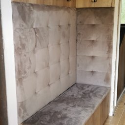 M N M Tomasz Dąbrowski - Kącik w przedpokoju z siedziskiem i wieszakami, obity beżową tapicerką z pikowaniem. Drewnopodobne wykończenie, czarne haczyki na ubrania.