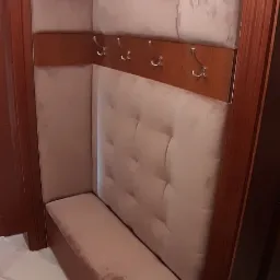 Tapicerowany przedpokój z siedziskiem, wnęką i wieszakami, utrzymany w beżowej kolorystyce, z widocznym fragmentem marmurowej podłogi i elementami garderoby na podłodze.