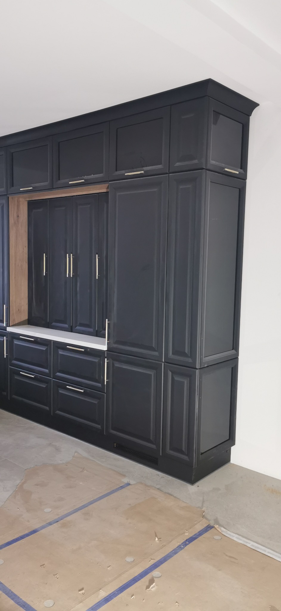 Czarne szafki kuchenne z frezowanymi frontami i długimi, srebrnymi uchwytami, z blatem w kolorze białym, podłoga zabezpieczona kartonem falistym.