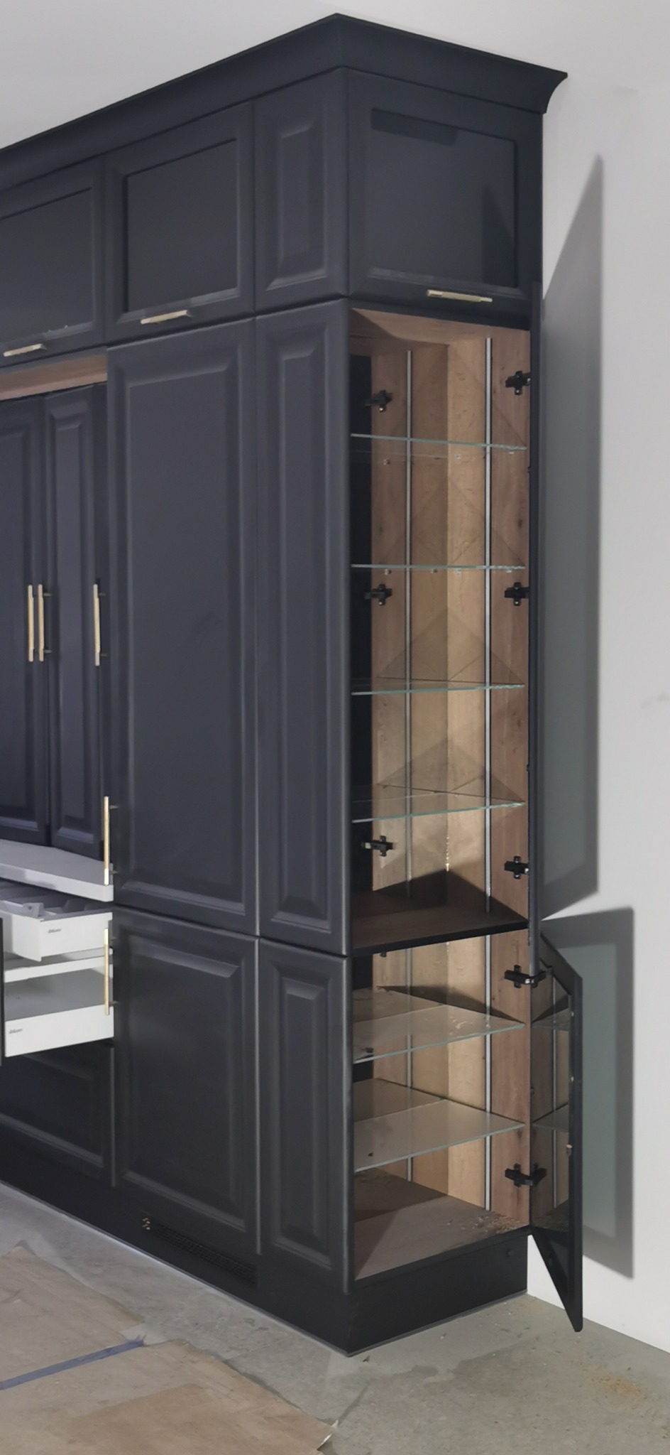 Ciemnoszara zabudowa meblowa z otwartą szafką z szklanymi półkami i wysuniętą szufladą, widoczne okucia Blum.