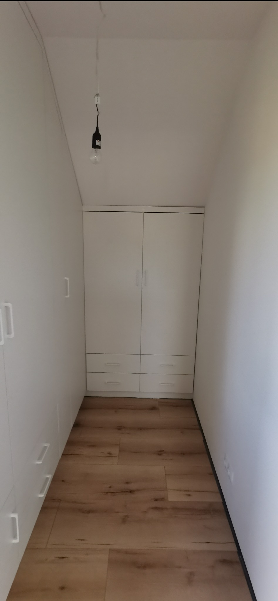 Biała szafa wnękowa z szufladami, idealnie dopasowana do wąskiego korytarza. Realizacja z Międzyrzecza. Minimalistyczny design, drewnopodobna podłoga.