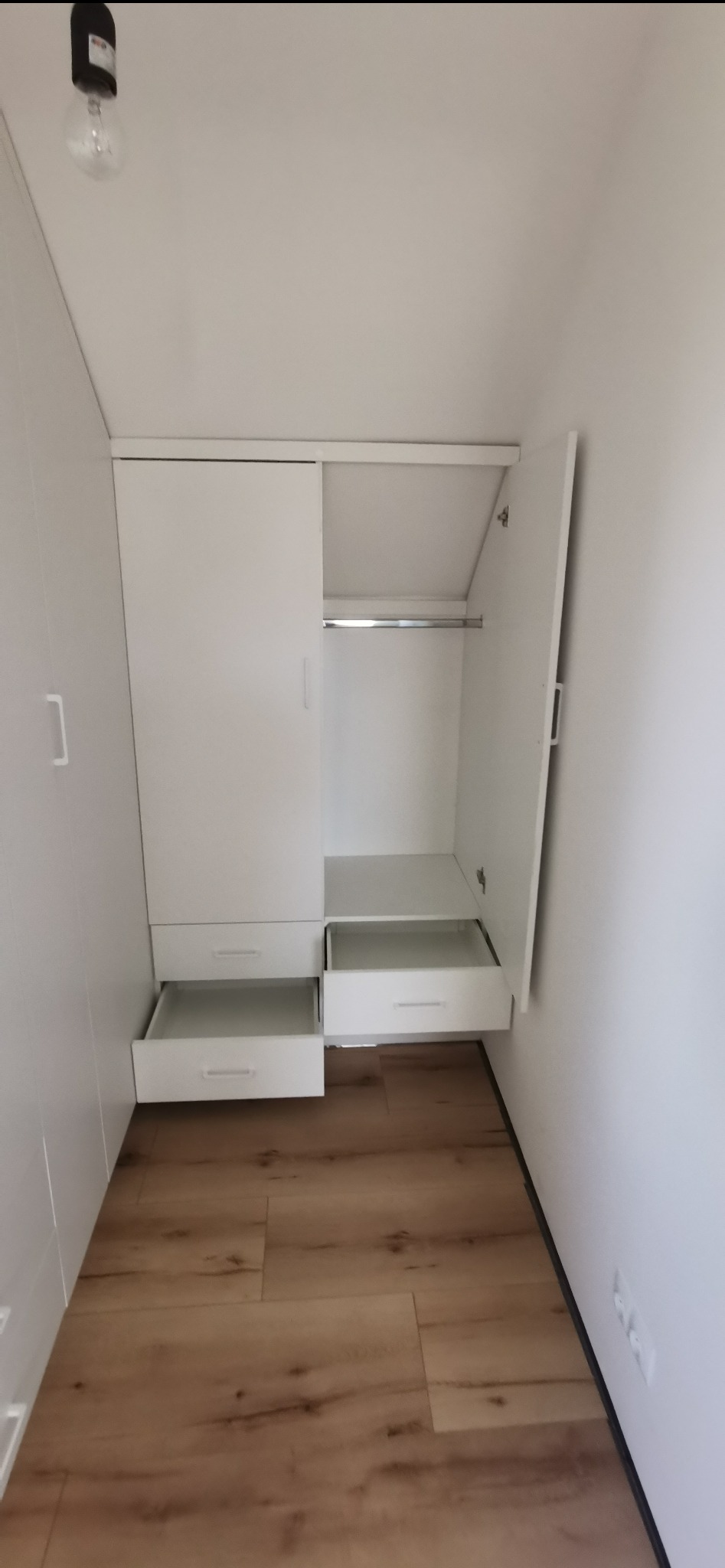 Biała szafa wnękowa z otwartymi drzwiami i wysuniętymi szufladami, widok z przodu na drewnianą podłogę, oświetlenie górne, minimalistyczny design.