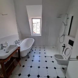 Biała łazienka na poddaszu z wanną na lwich nóżkach, umywalką na drewnianym stelażu i kabiną prysznicową typu walk-in.