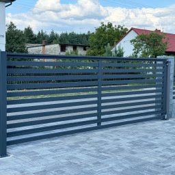 STALIAS Krystian Białas - Nowoczesna, przesuwna brama wjazdowa w kolorze antracytowym z poziomymi panelami, zamontowana na posesji z szarej kostki brukowej i betonowych słupków.