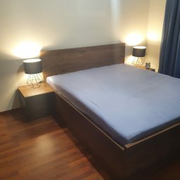 Meble BONCI - Nowoczesne łóżko z drewnianym wezgłowiem i szafkami nocnymi z geometrycznymi lampkami, oświetlone ciepłym światłem, na parkiecie.