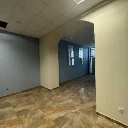 Wnętrze biura z podłogą wyłożoną brązowymi płytkami imitującymi marmur, niebieskimi ścianami i sufitem kasetonowym z otwartym panelem świetlnym.